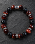 Men's 10mm striped black Onyx and Red Tiger Eye bracelet with silver-tone spacers and barrel centerpiece against charcoal slate